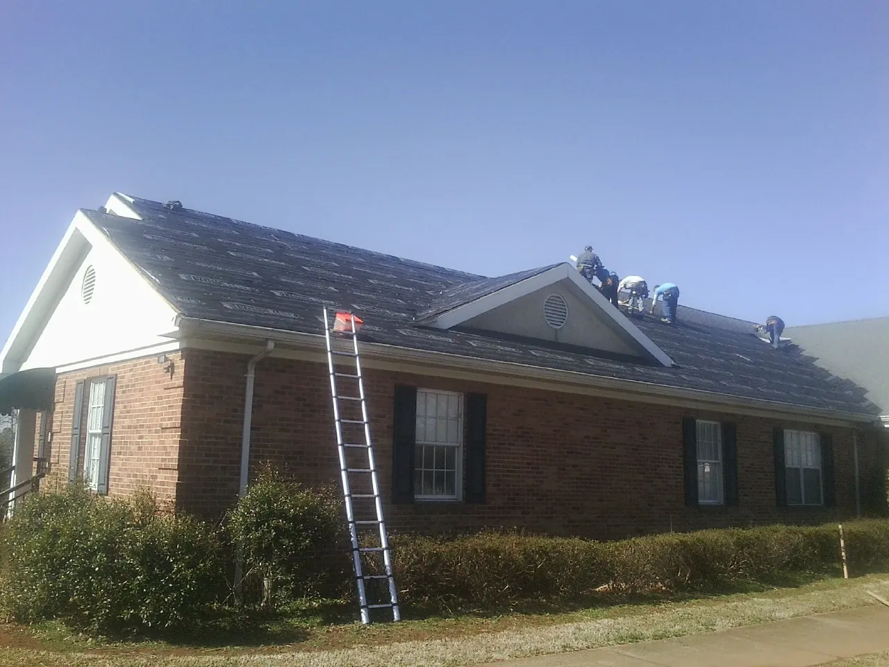 Crew tearing shingles off a brick ranch roof with a ladder set — Metal Roof Repair work by our crew in Irvington
