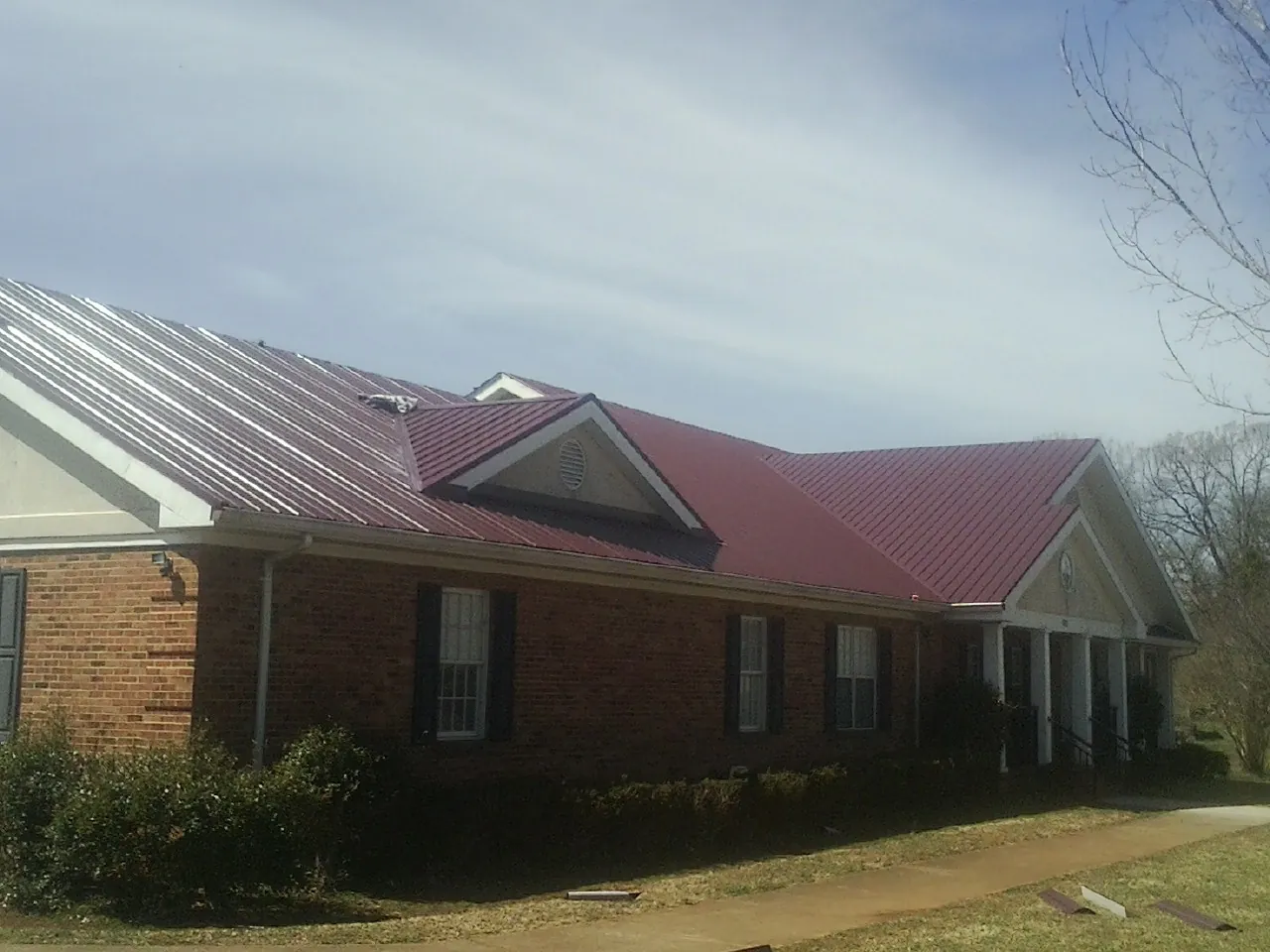 Red metal roof with gabled entries on a long brick building, from a Hail Damage Roof Repair job in Irvington