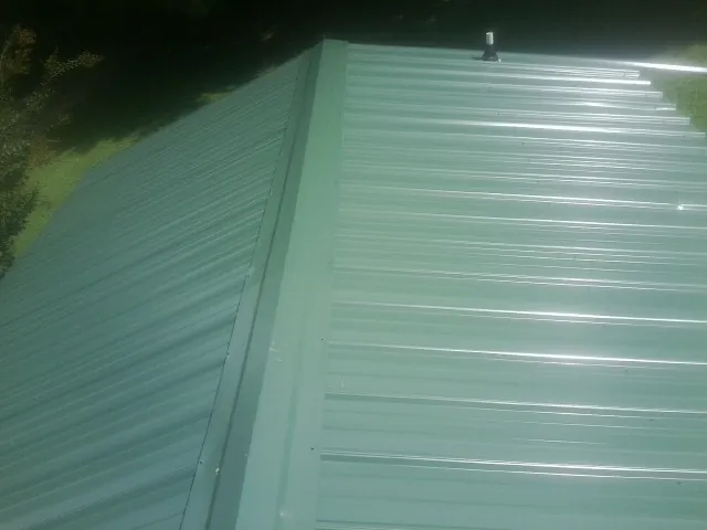 New green metal panels meeting at the ridge of a roof — Flat Roof Repair work by our crew in Irvington