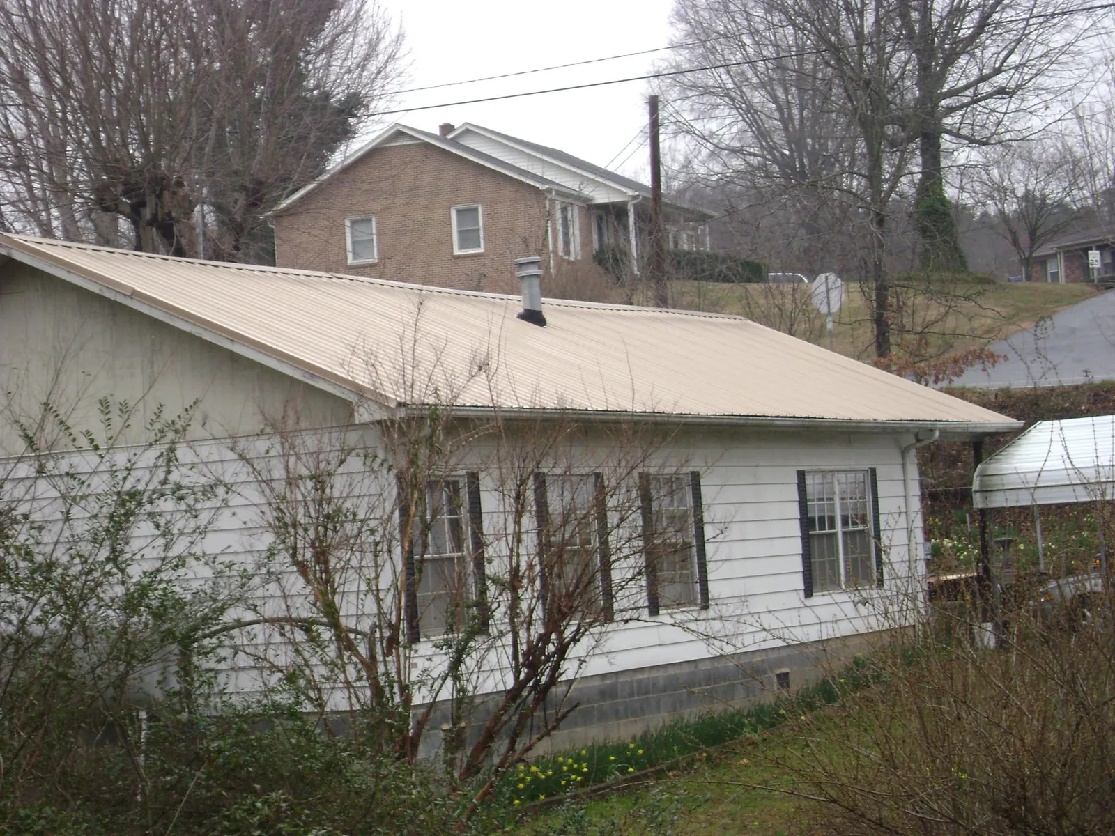 Tan metal roof on a white sided house set into a hillside — Commercial Roofing by Roofing Brothers in Irvington